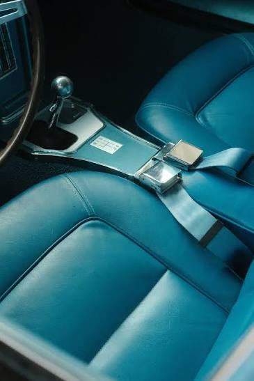 Classic car interior in turquoise leather with chrome lap belt buckles fitted across the bench seat.