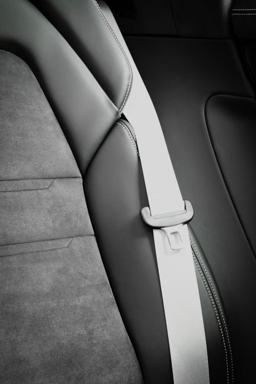 Light grey seat belt webbing and matching latch plate running down the side of a dark vehicle seat.