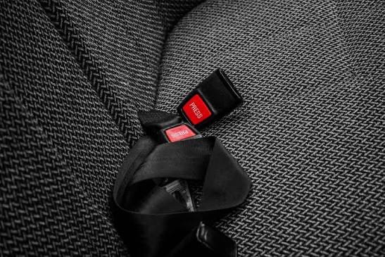 Two seat belt buckle stalks with red press-release buttons, fitted on a grey fabric vehicle seat.