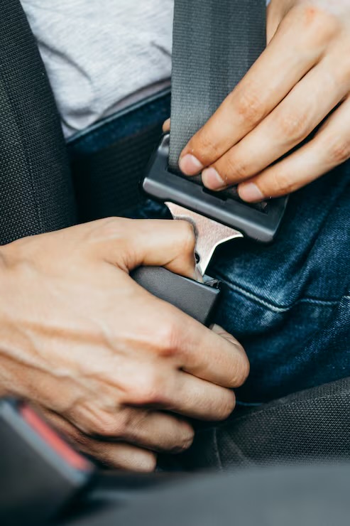 Two hands guiding a seat belt latch plate into the buckle, with the chrome tongue aligned at the buckle throat.